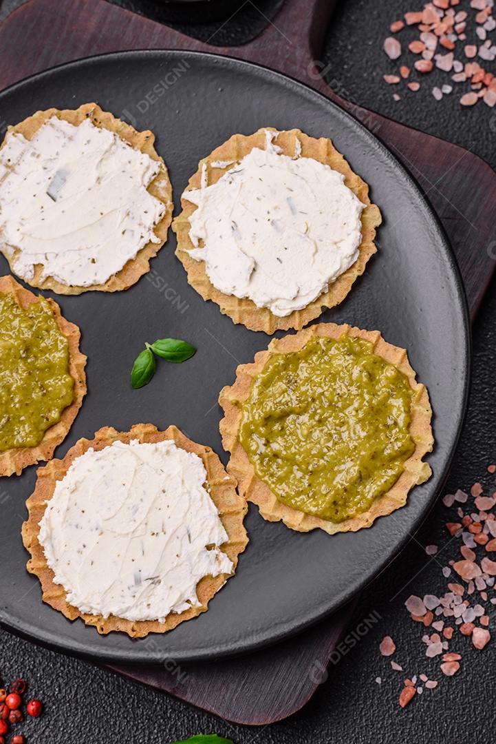 Petiscos redondos com chips crocantes ou biscoitos com cream cheese e pesto num prato de cerâmica