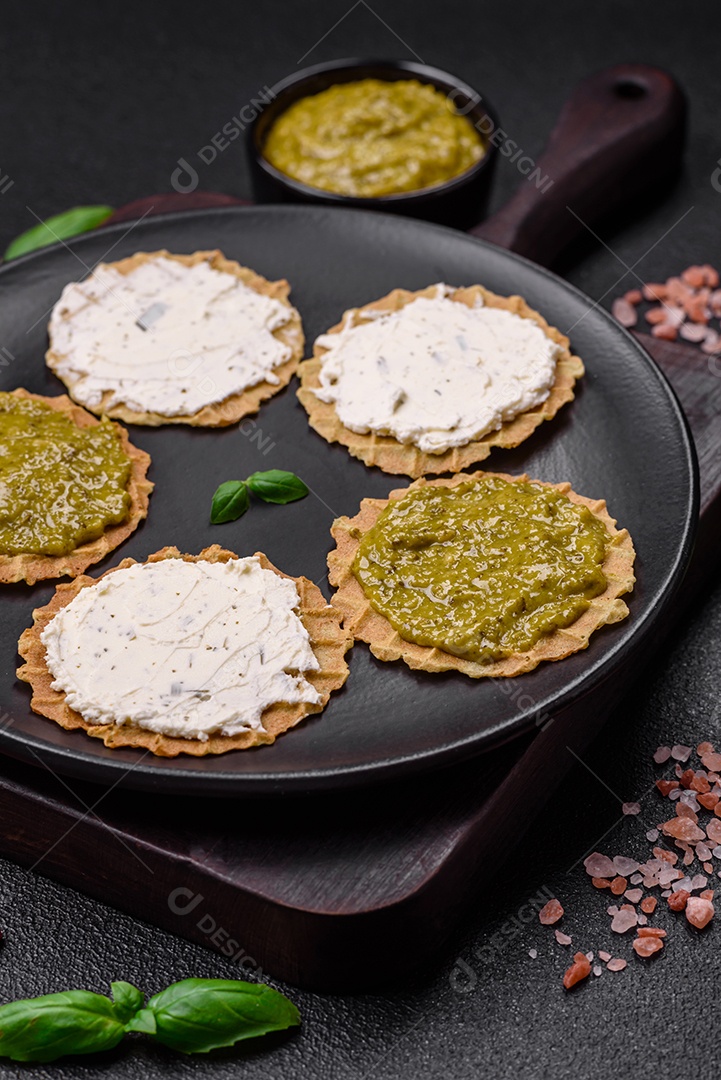 Petiscos redondos com chips crocantes ou biscoitos com cream cheese e pesto num prato de cerâmica