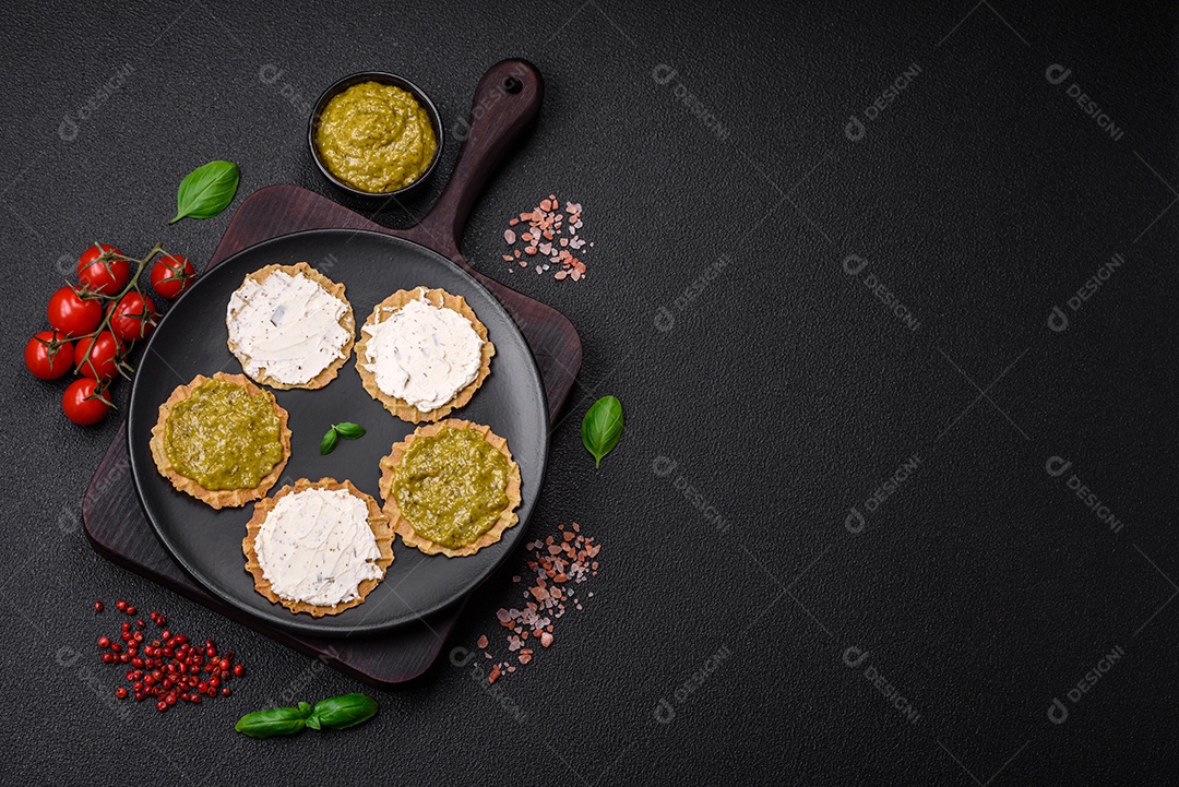 Petiscos redondos com chips crocantes ou biscoitos com cream cheese e pesto num prato de cerâmica