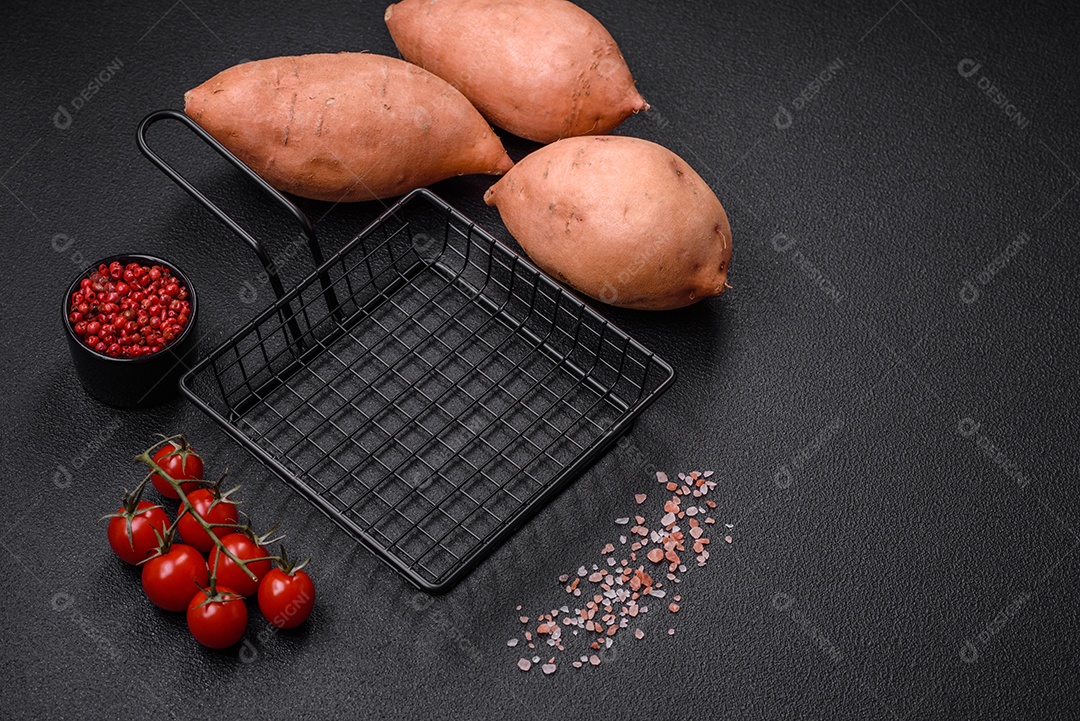 Grandes tubérculos frescos de batata-doce rosa com tomates e especiarias em um fundo escuro. Cozinhando uma refeição vegetariana saudável