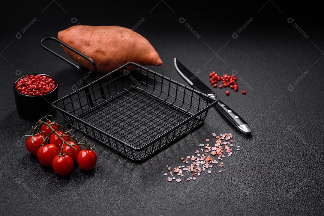 Grandes tubérculos frescos de batata-doce rosa com tomates e especiarias em um fundo escuro. Cozinhando uma refeição vegetariana saudável