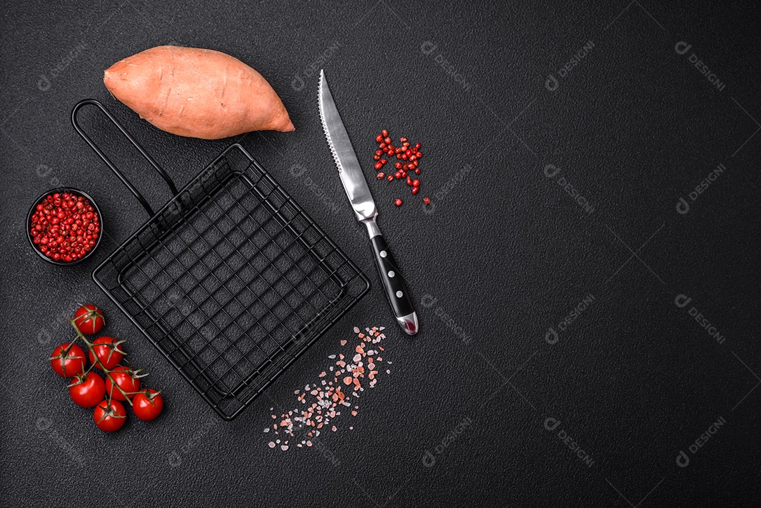 Grandes tubérculos frescos de batata-doce rosa com tomates e especiarias em um fundo escuro. Cozinhando uma refeição vegetariana saudável