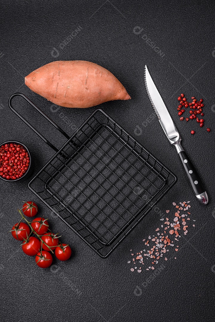 Grandes tubérculos frescos de batata-doce rosa com tomates e especiarias em um fundo escuro. Cozinhando uma refeição vegetariana saudável