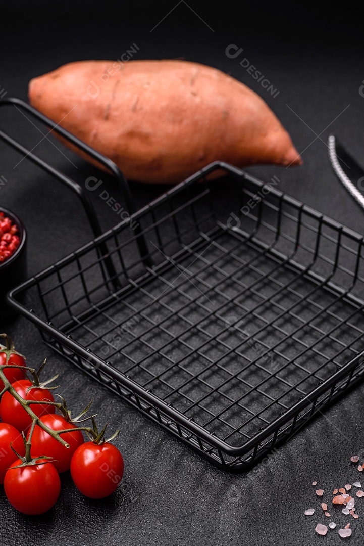 Grandes tubérculos frescos de batata-doce rosa com tomates e especiarias em um fundo escuro. Cozinhando uma refeição vegetariana saudável