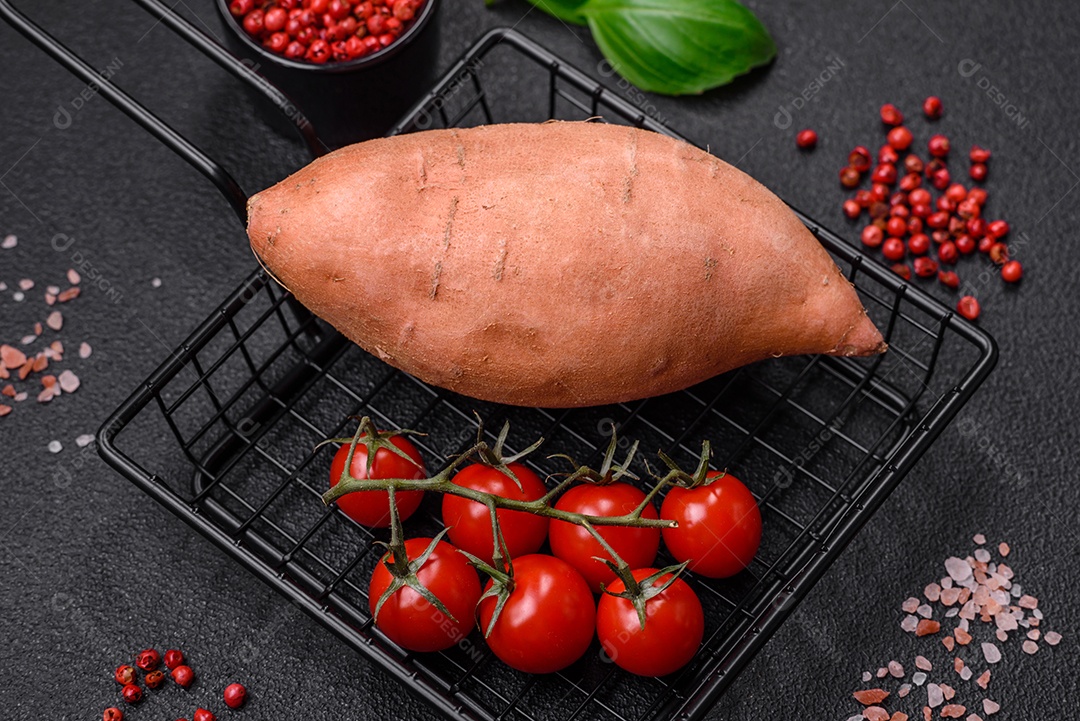 Grandes tubérculos frescos de batata-doce rosa com tomates e especiarias em um fundo escuro. Cozinhando uma refeição vegetariana saudável