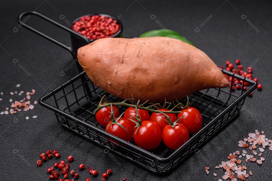 Grandes tubérculos frescos de batata-doce rosa com tomates e especiarias em um fundo escuro. Cozinhando uma refeição vegetariana saudável