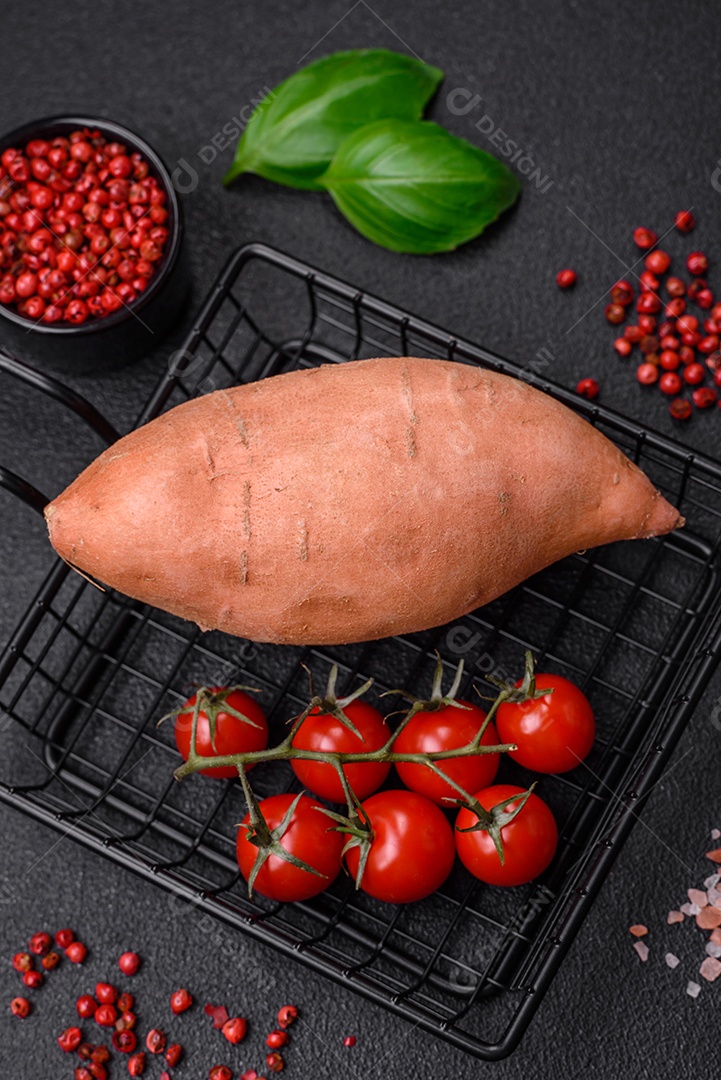 Grandes tubérculos frescos de batata-doce rosa com tomates e especiarias em um fundo escuro. Cozinhando uma refeição vegetariana saudável