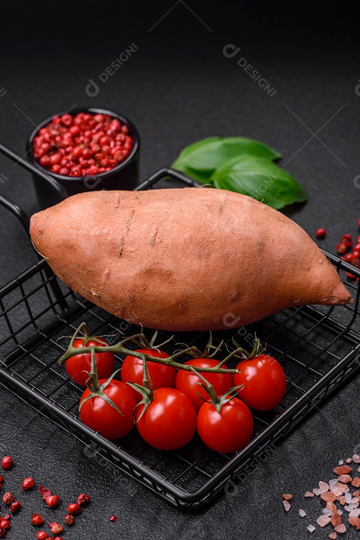 Grandes tubérculos frescos de batata-doce rosa com tomates e especiarias em um fundo escuro. Cozinhando uma refeição vegetariana saudável