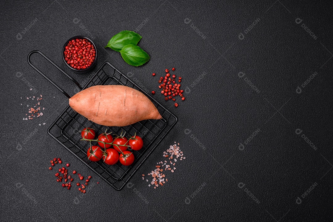 Grandes tubérculos frescos de batata-doce rosa com tomates e especiarias em um fundo escuro. Cozinhando uma refeição vegetariana saudável