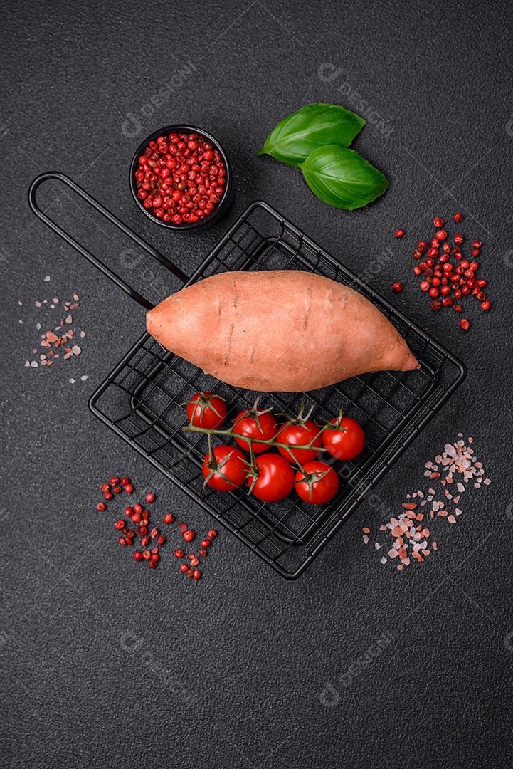 Grandes tubérculos frescos de batata-doce rosa com tomates e especiarias em um fundo escuro. Cozinhando uma refeição vegetariana saudável