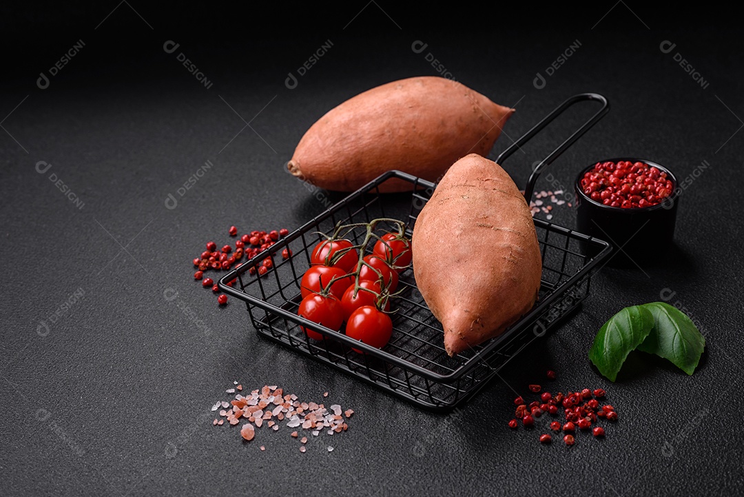 Grandes tubérculos frescos de batata-doce rosa com tomates e especiarias em um fundo escuro. Cozinhando uma refeição vegetariana saudável