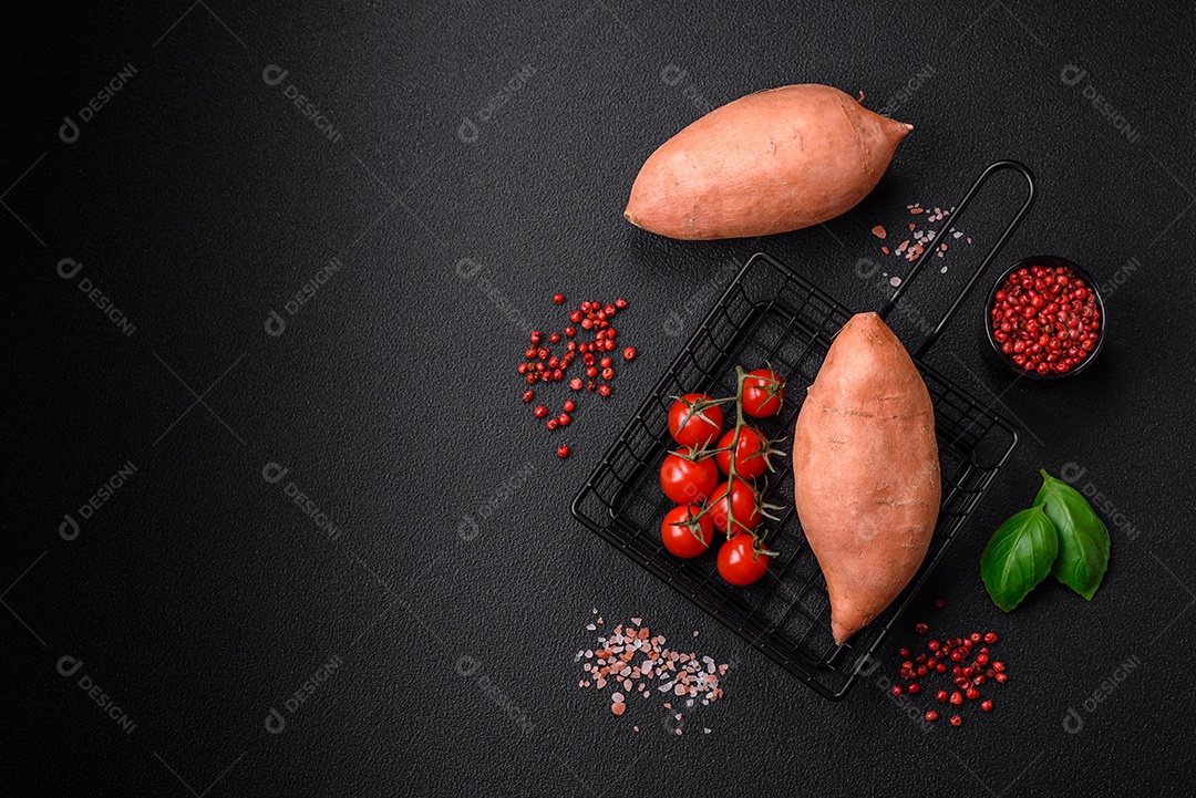 Grandes tubérculos frescos de batata-doce rosa com tomates e especiarias em um fundo escuro. Cozinhando uma refeição vegetariana saudável