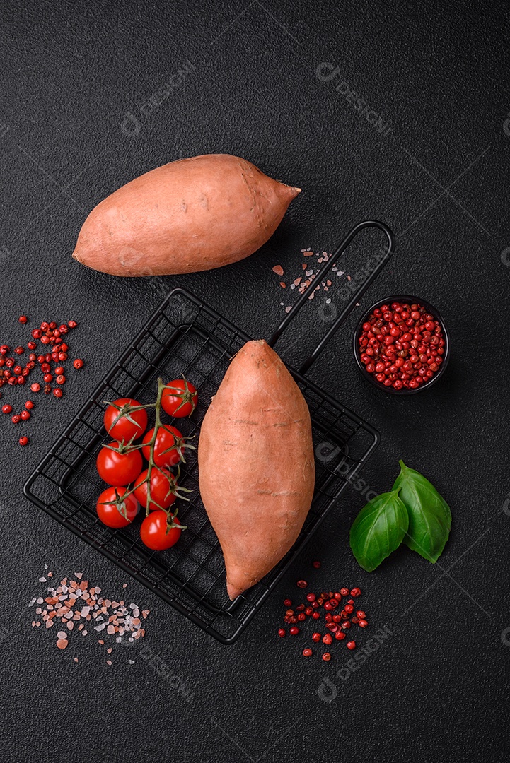 Grandes tubérculos frescos de batata-doce rosa com tomates e especiarias em um fundo escuro. Cozinhando uma refeição vegetariana saudável