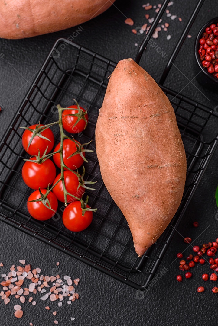 Grandes tubérculos frescos de batata-doce rosa com tomates e especiarias em um fundo escuro. Cozinhando uma refeição vegetariana saudável