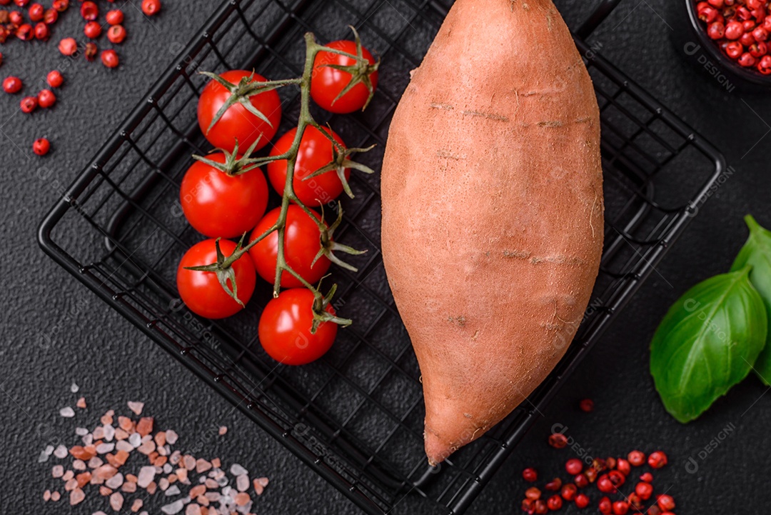 Grandes tubérculos frescos de batata-doce rosa com tomates e especiarias em um fundo escuro. Cozinhando uma refeição vegetariana saudável