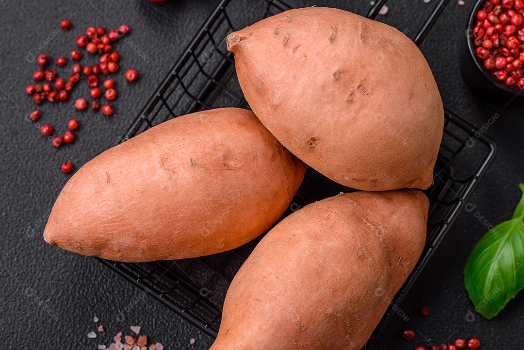 Grandes tubérculos frescos de batata-doce rosa com tomates e especiarias em um fundo escuro. Cozinhando uma refeição vegetariana saudável