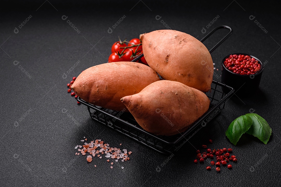 Grandes tubérculos frescos de batata-doce rosa com tomates e especiarias em um fundo escuro. Cozinhando uma refeição vegetariana saudável