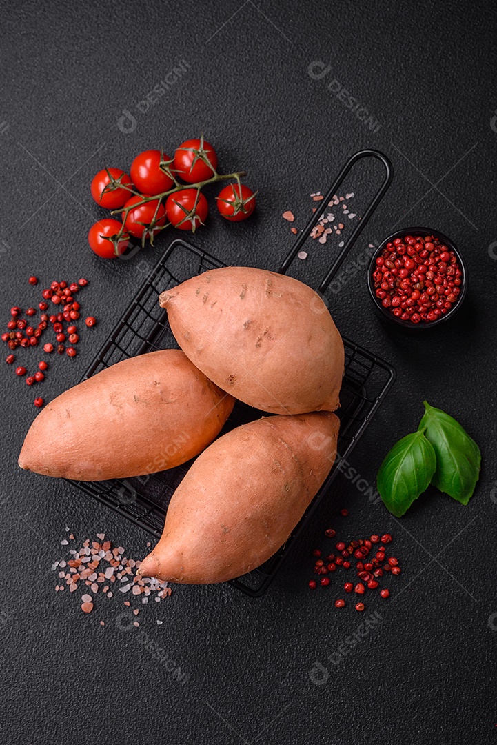 Grandes tubérculos frescos de batata-doce rosa com tomates e especiarias em um fundo escuro. Cozinhando uma refeição vegetariana saudável