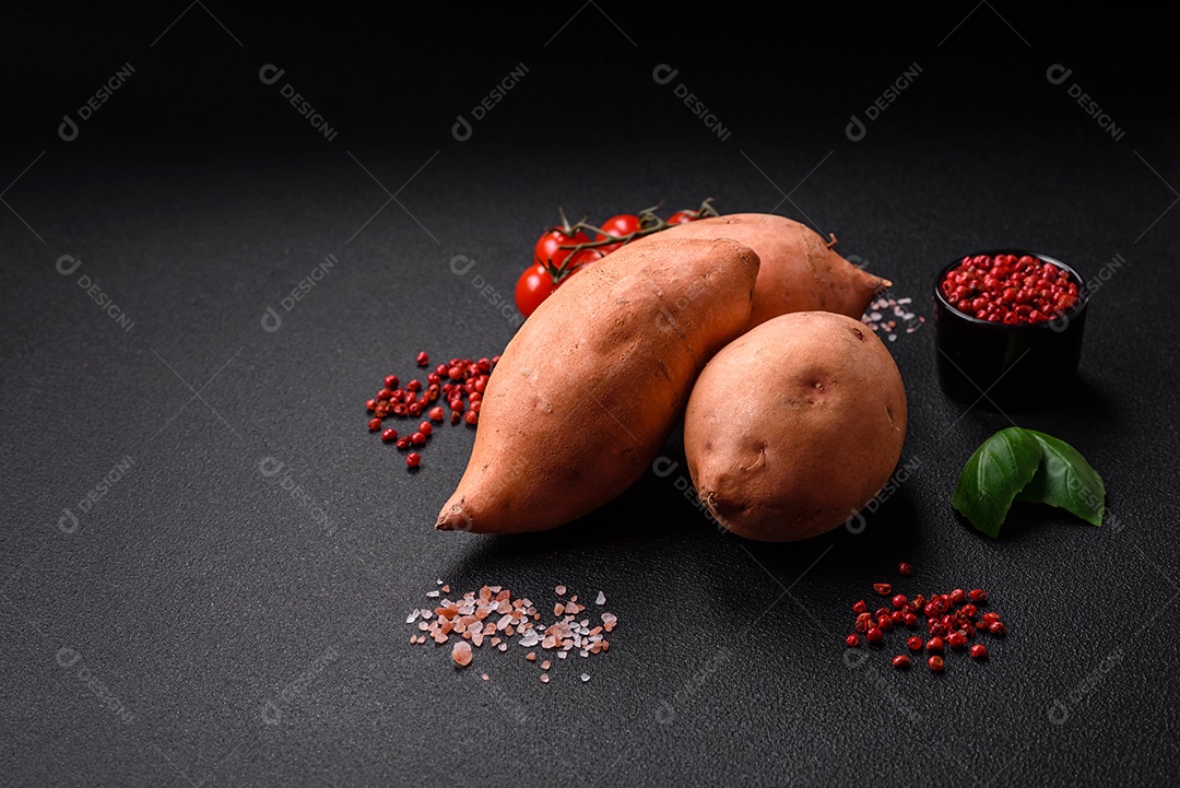 Grandes tubérculos frescos de batata-doce rosa com tomates e especiarias em um fundo escuro. Cozinhando uma refeição vegetariana saudável