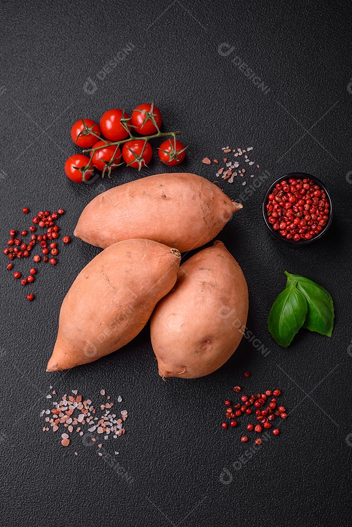 Grandes tubérculos frescos de batata-doce rosa com tomates e especiarias em um fundo escuro. Cozinhando uma refeição vegetariana saudável