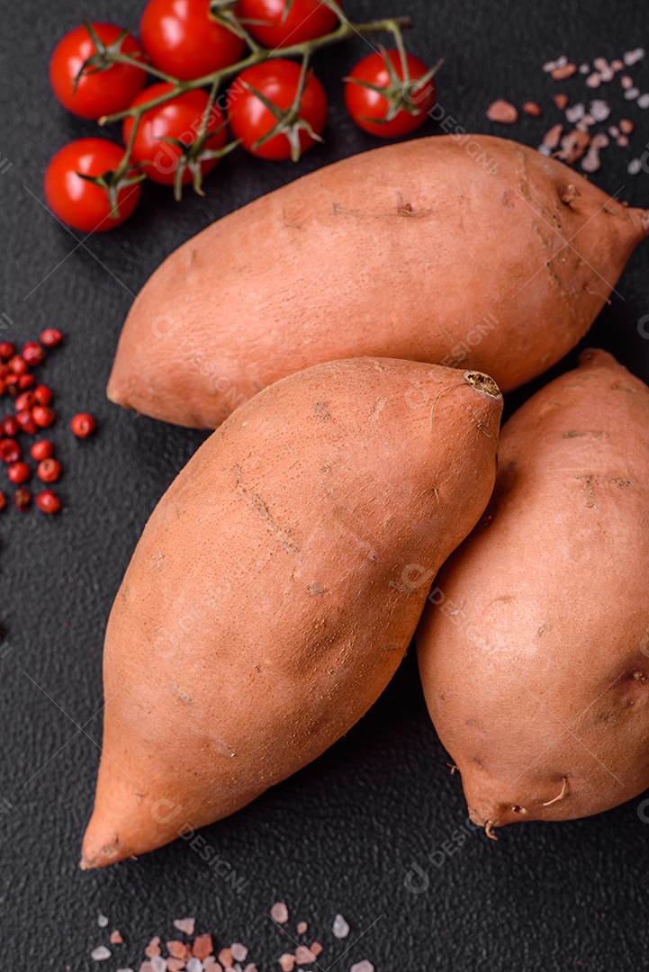 Grandes tubérculos frescos de batata-doce rosa com tomates e especiarias em um fundo escuro. Cozinhando uma refeição vegetariana saudável