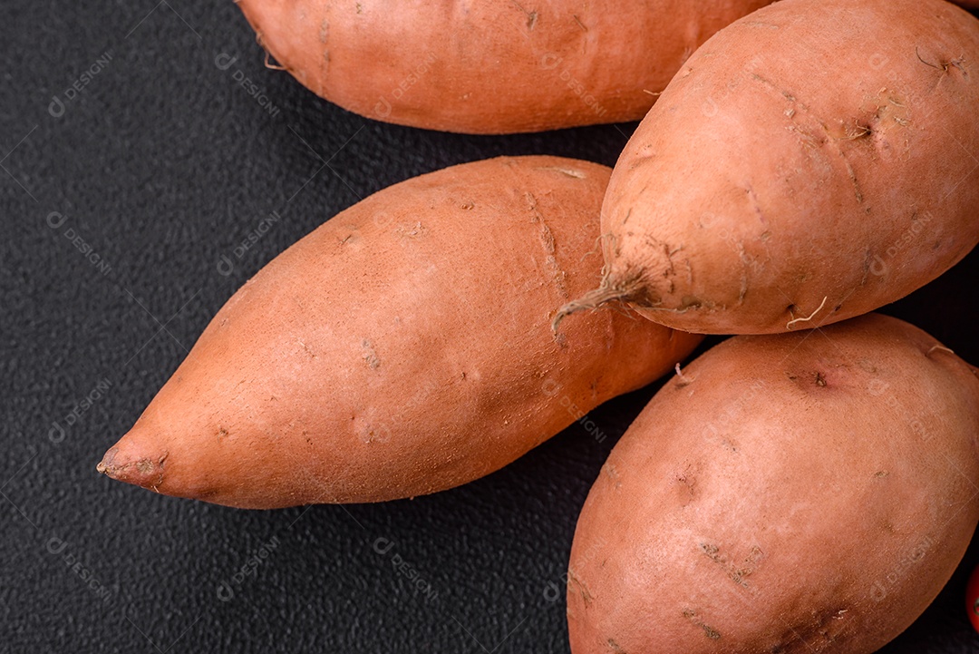 Grandes tubérculos frescos de batata-doce rosa com tomates e especiarias em um fundo escuro. Cozinhando uma refeição vegetariana saudável