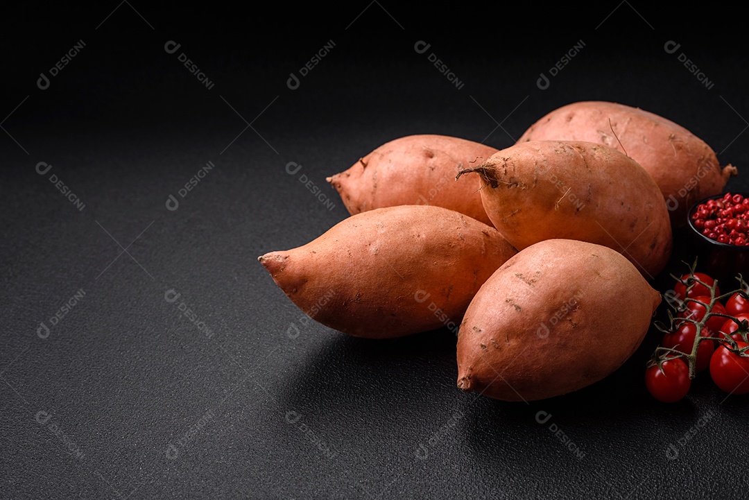 Grandes tubérculos frescos de batata-doce rosa com tomates e especiarias em um fundo escuro. Cozinhando uma refeição vegetariana saudável
