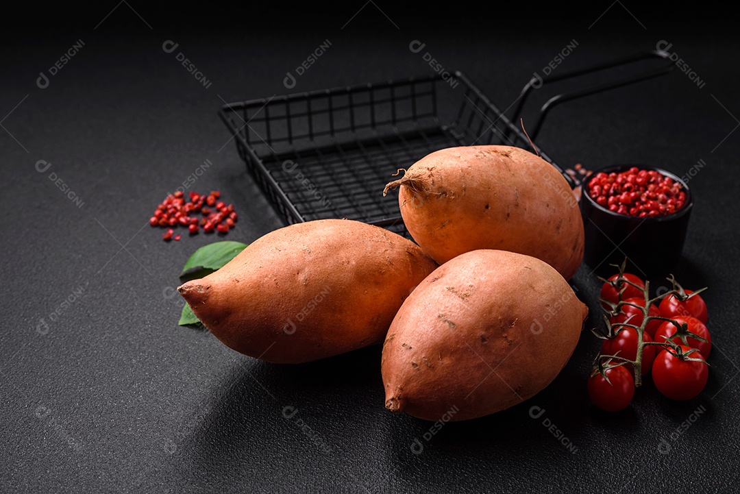 Grandes tubérculos frescos de batata-doce rosa com tomates e especiarias em um fundo escuro. Cozinhando uma refeição vegetariana saudável