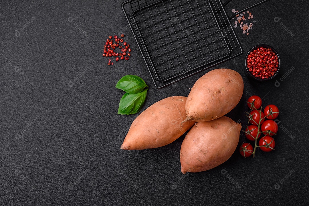 Grandes tubérculos frescos de batata-doce rosa com tomates e especiarias em um fundo escuro. Cozinhando uma refeição vegetariana saudável