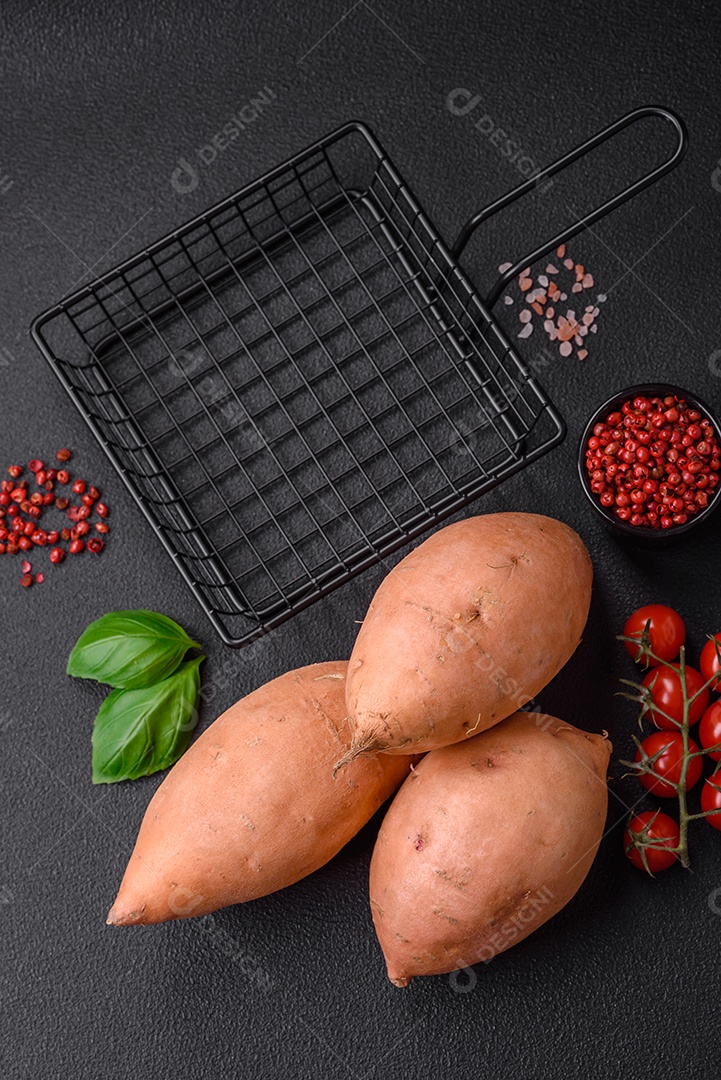 Grandes tubérculos frescos de batata-doce rosa com tomates e especiarias em um fundo escuro. Cozinhando uma refeição vegetariana saudável