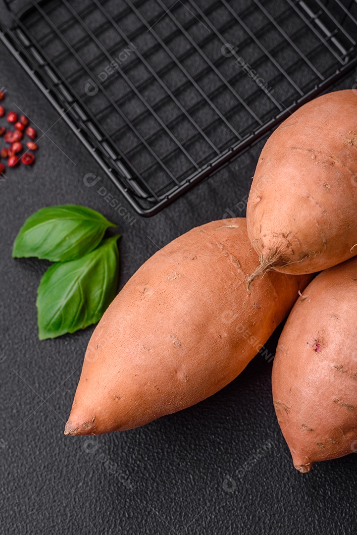Grandes tubérculos frescos de batata-doce rosa com tomates e especiarias em um fundo escuro. Cozinhando uma refeição vegetariana saudável