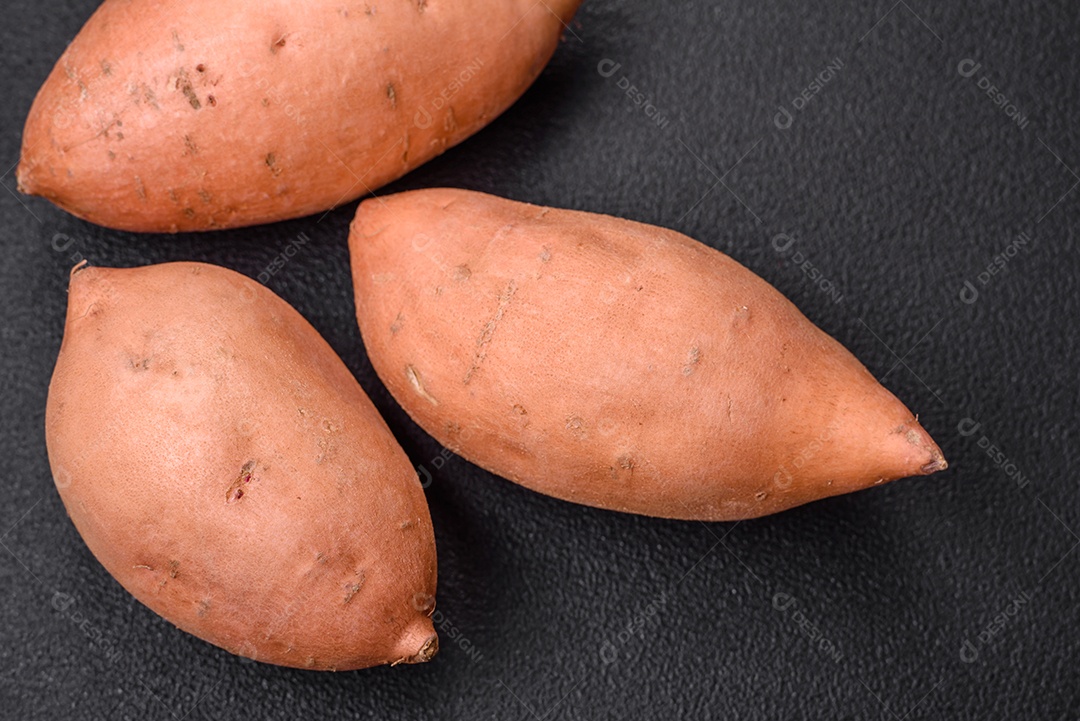 Grandes tubérculos frescos de batata-doce rosa com tomates e especiarias em um fundo escuro. Cozinhando uma refeição vegetariana saudável