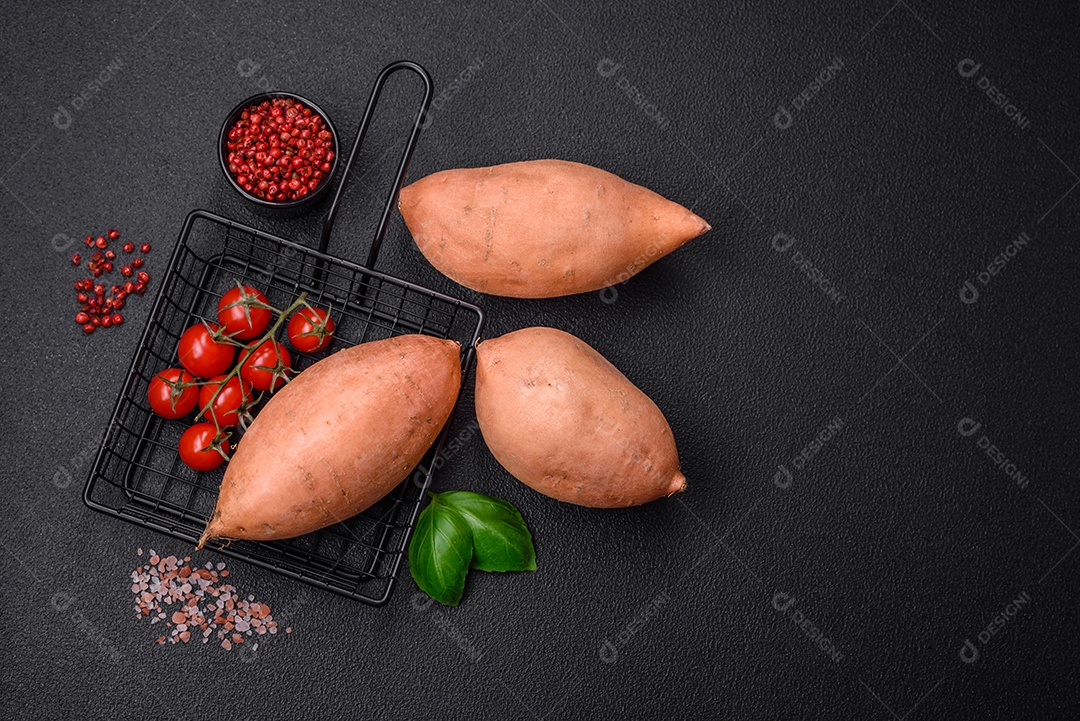 Grandes tubérculos frescos de batata-doce rosa com tomates e especiarias em um fundo escuro. Cozinhando uma refeição vegetariana saudável