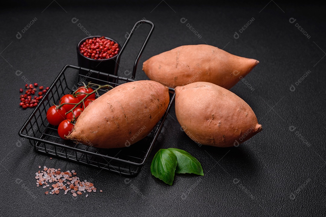 Grandes tubérculos frescos de batata-doce rosa com tomates e especiarias em um fundo escuro. Cozinhando uma refeição vegetariana saudável