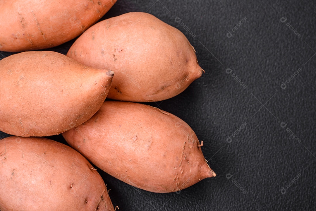 Grandes tubérculos frescos de batata-doce rosa com tomates e especiarias em um fundo escuro. Cozinhando uma refeição vegetariana saudável