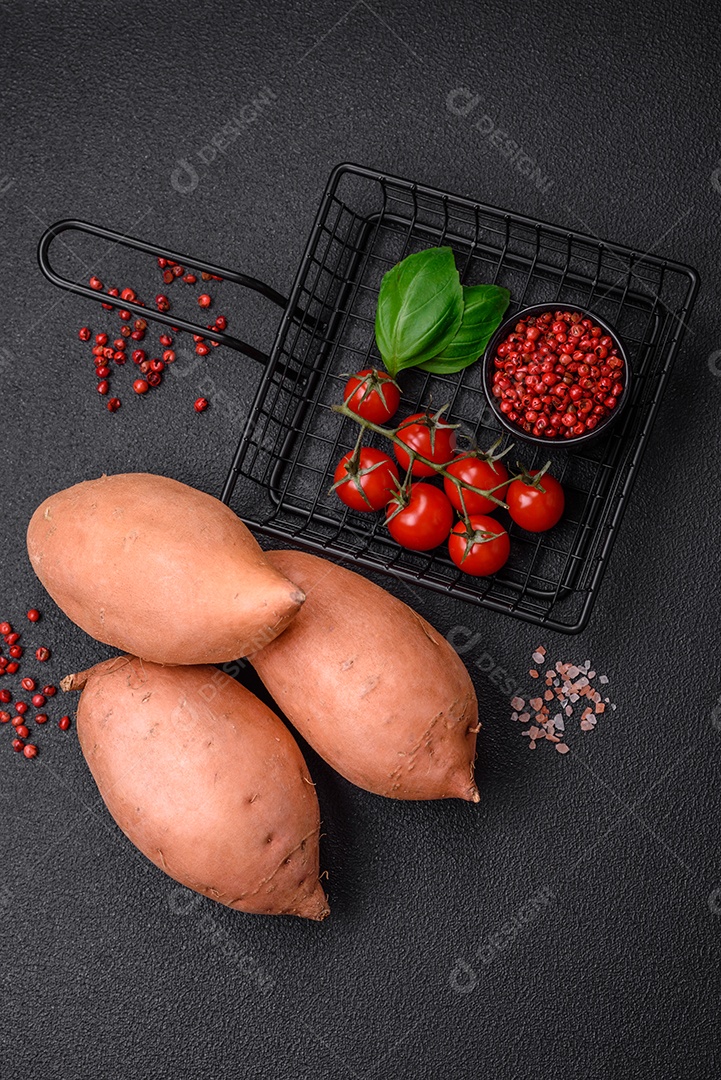 Grandes tubérculos frescos de batata-doce rosa com tomates e especiarias em um fundo escuro. Cozinhando uma refeição vegetariana saudável