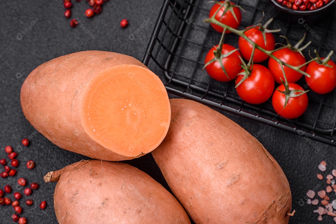 Grandes tubérculos frescos de batata-doce rosa com tomates e especiarias em um fundo escuro. Cozinhando uma refeição vegetariana saudável