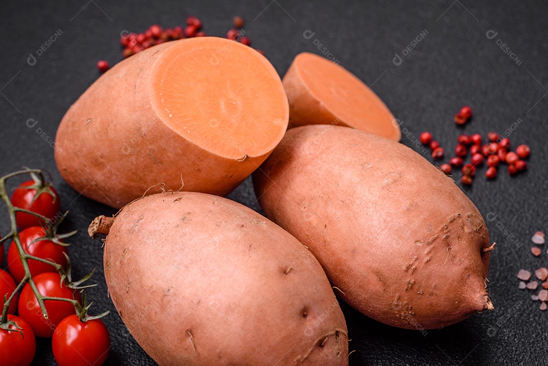 Grandes tubérculos frescos de batata-doce rosa com tomates e especiarias em um fundo escuro. Cozinhando uma refeição vegetariana saudável