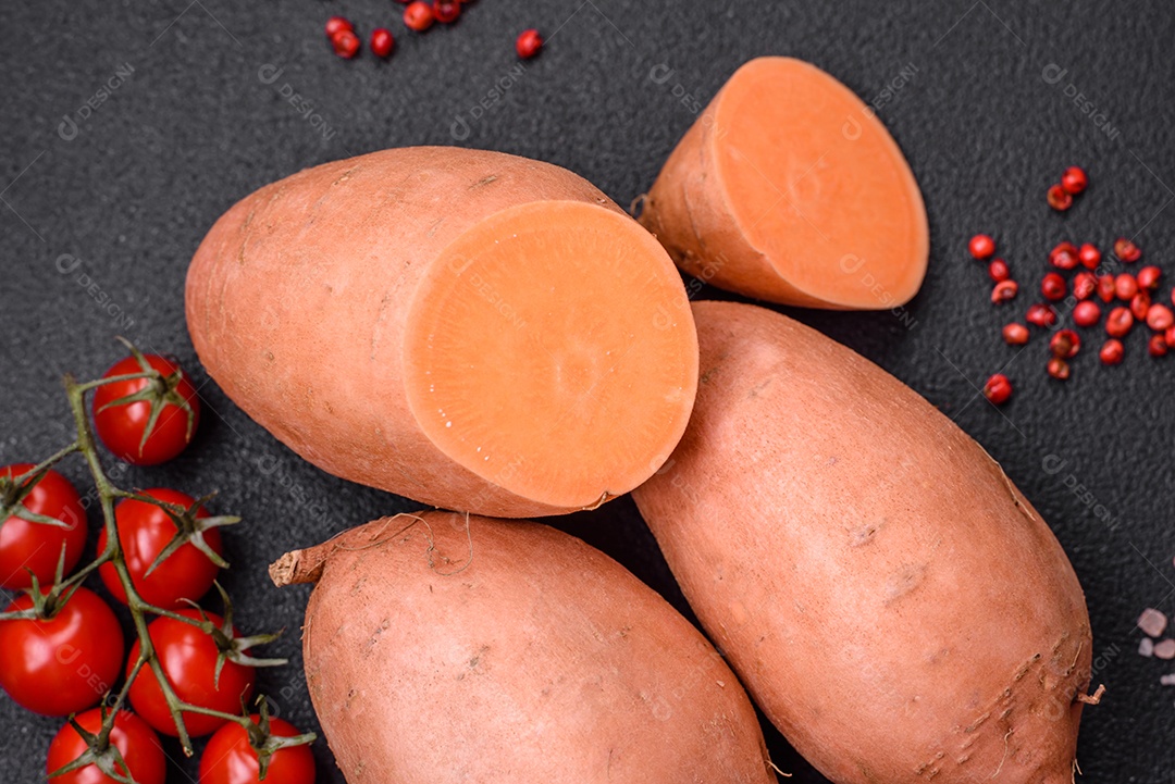 Grandes tubérculos frescos de batata-doce rosa com tomates e especiarias em um fundo escuro. Cozinhando uma refeição vegetariana saudável