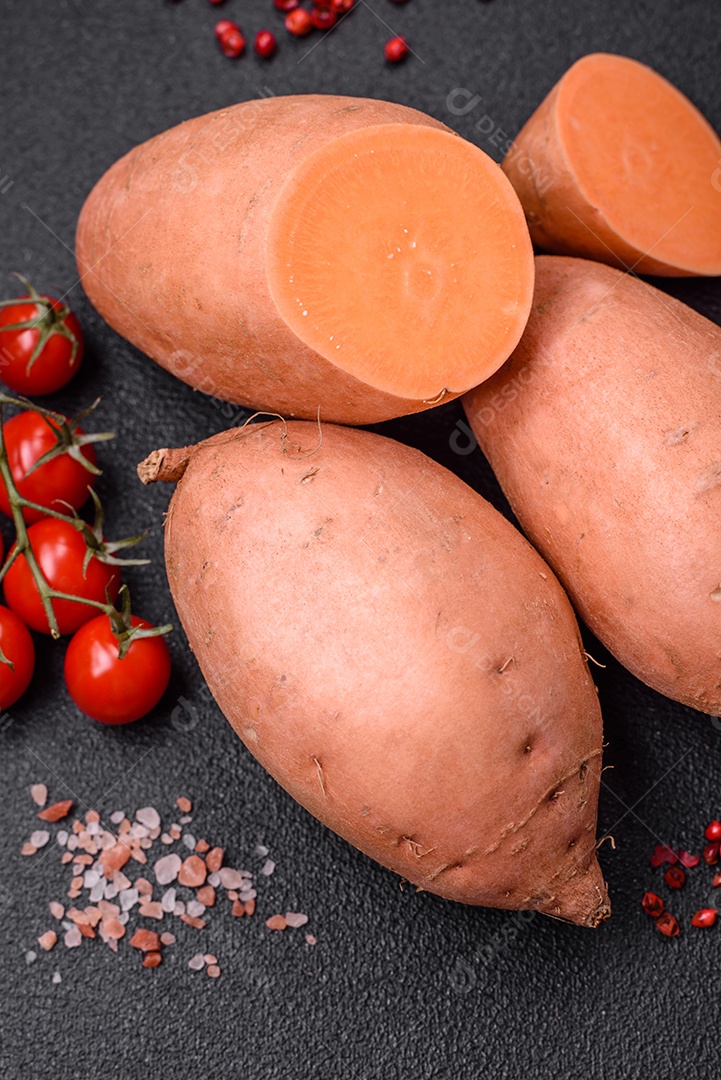 Grandes tubérculos frescos de batata-doce rosa com tomates e especiarias em um fundo escuro. Cozinhando uma refeição vegetariana saudável