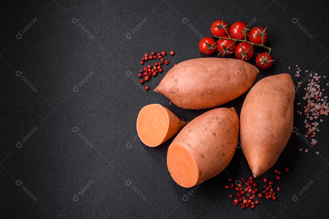 Grandes tubérculos frescos de batata-doce rosa com tomates e especiarias em um fundo escuro. Cozinhando uma refeição vegetariana saudável