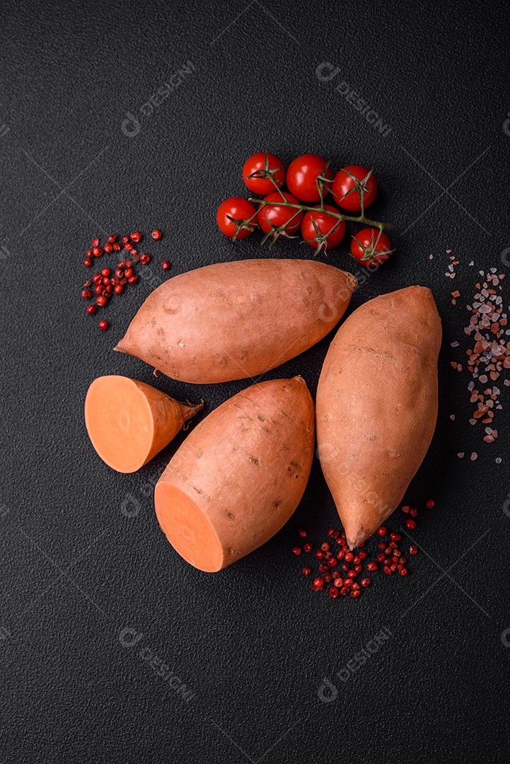 Grandes tubérculos frescos de batata-doce rosa com tomates e especiarias em um fundo escuro. Cozinhando uma refeição vegetariana saudável