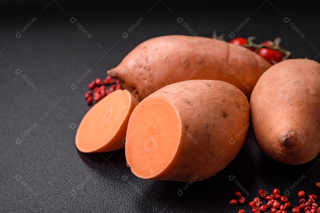 Grandes tubérculos frescos de batata-doce rosa com tomates e especiarias em um fundo escuro. Cozinhando uma refeição vegetariana saudável