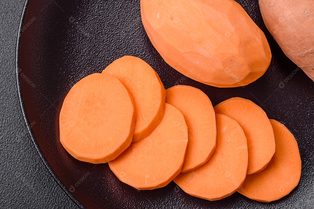 Grandes tubérculos frescos de batata-doce rosa com tomates e especiarias em um fundo escuro. Cozinhando uma refeição vegetariana saudável