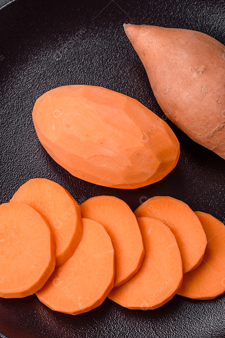 Grandes tubérculos frescos de batata-doce rosa com tomates e especiarias em um fundo escuro. Cozinhando uma refeição vegetariana saudável