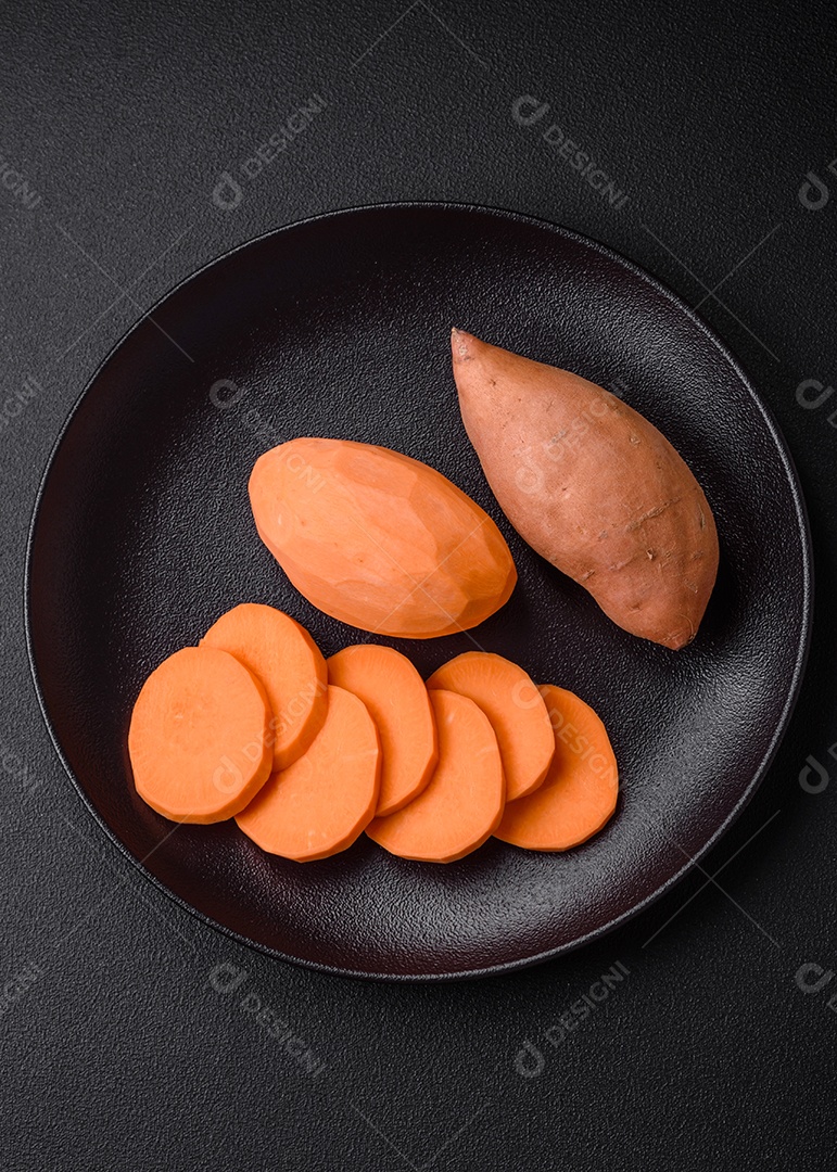 Grandes tubérculos frescos de batata-doce rosa com tomates e especiarias em um fundo escuro. Cozinhando uma refeição vegetariana saudável