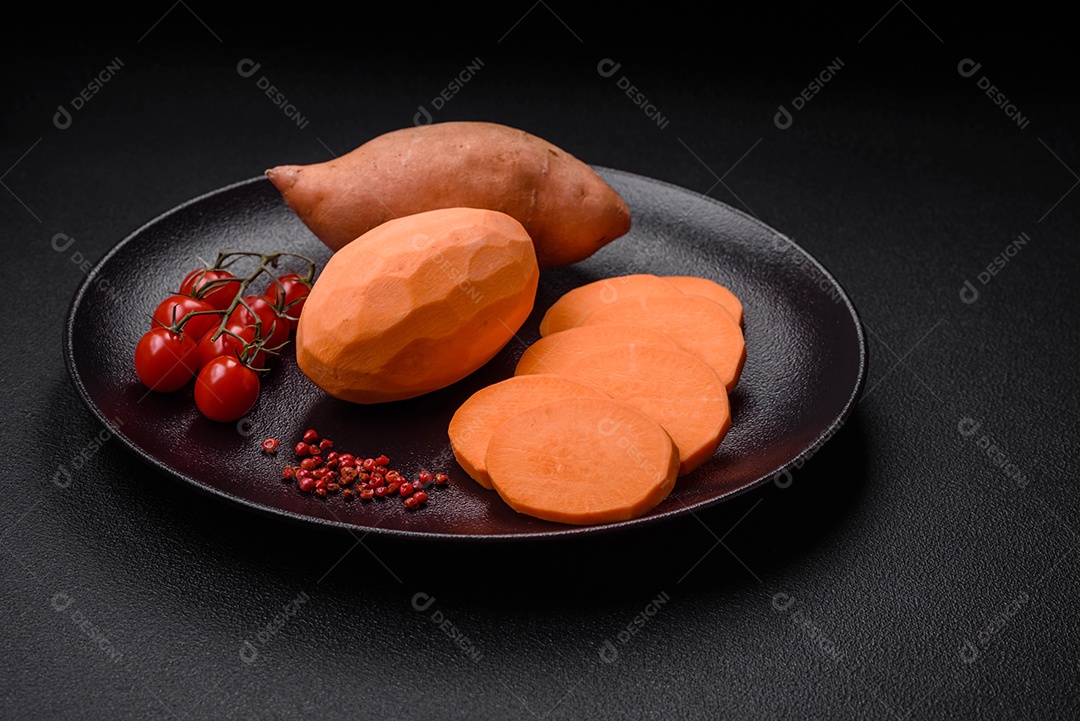 Grandes tubérculos frescos de batata-doce rosa com tomates e especiarias em um fundo escuro. Cozinhando uma refeição vegetariana saudável