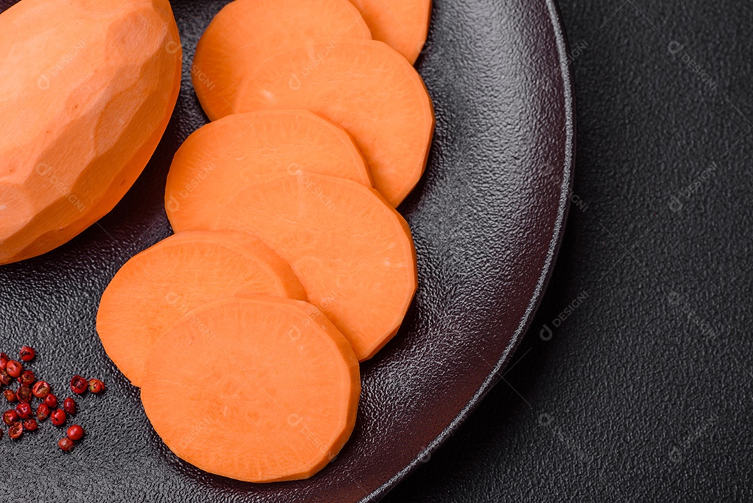 Grandes tubérculos frescos de batata-doce rosa com tomates e especiarias em um fundo escuro. Cozinhando uma refeição vegetariana saudável