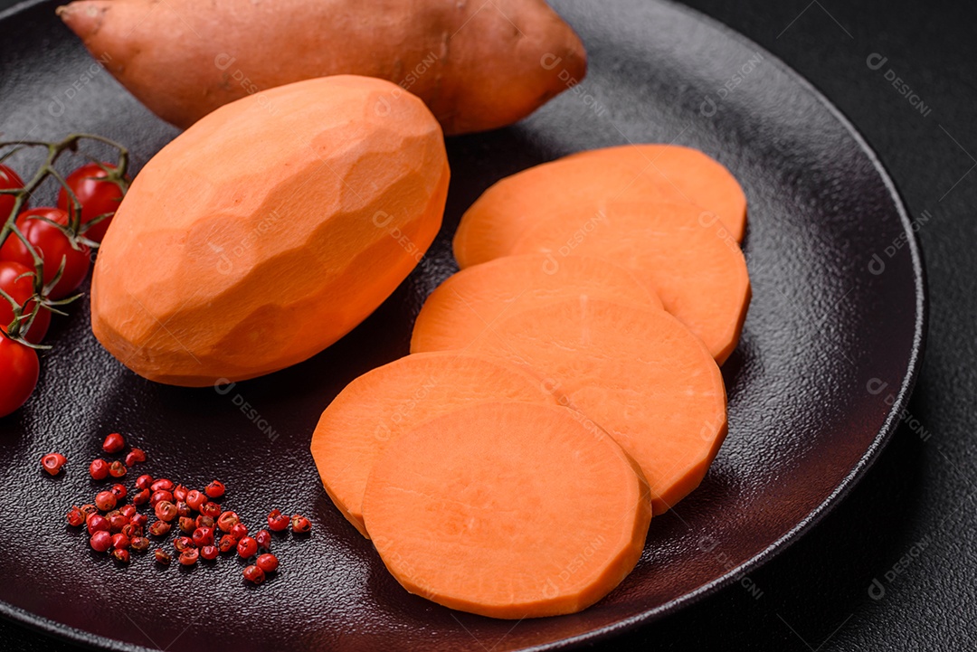 Grandes tubérculos frescos de batata-doce rosa com tomates e especiarias em um fundo escuro. Cozinhando uma refeição vegetariana saudável