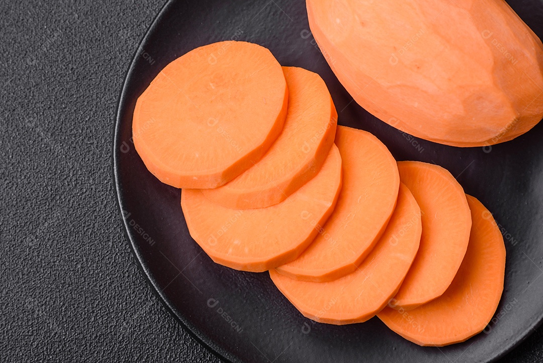 Grandes tubérculos frescos de batata-doce rosa com tomates e especiarias em um fundo escuro. Cozinhando uma refeição vegetariana saudável